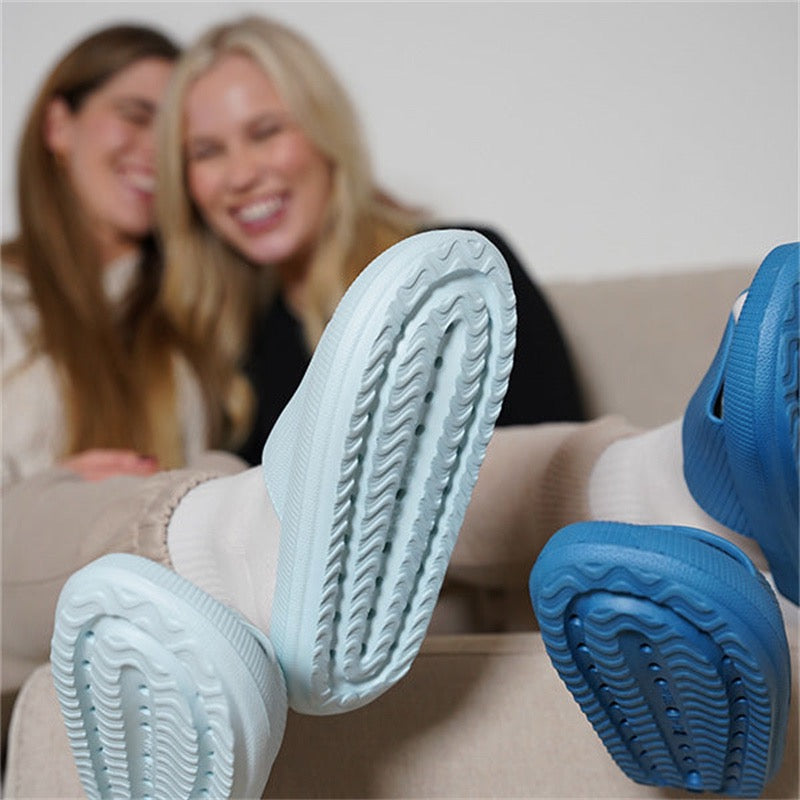 Two friends laughing on a sofa with their Puffy Slide soles toward the camera